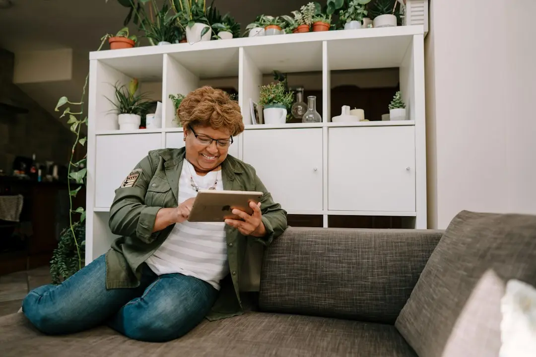 A woman using a tablet while sitting against a couch, a device that can run an IPTV player for Mediaspelare