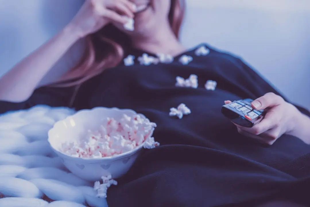 A person eating popcorn on the couch with a remote in hand, watching Mediaspelare in TiviMate